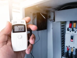 Close-up of a hand using a temperature data logger next to another machine.
