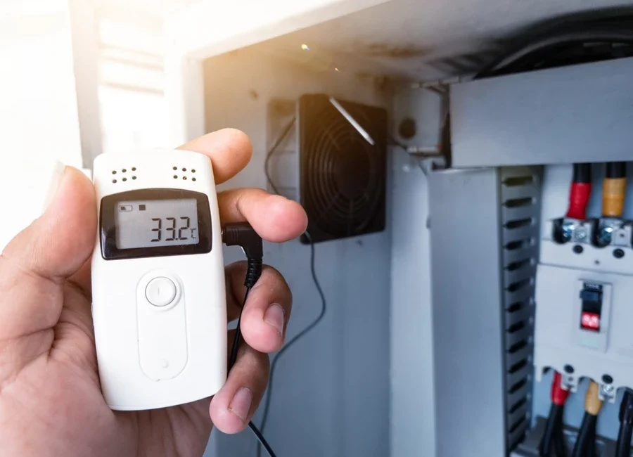 Close-up of a hand using a temperature data logger next to another machine.