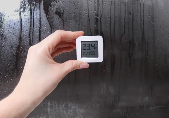 A digital temperature and humidity reading with a condensation-soaked mirror or window in the background.