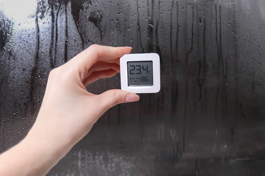 A digital temperature and humidity reading with a condensation-soaked mirror or window in the background.